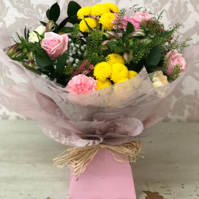 Sweet Surprise - A delightful mix of pinks, yellows, and whites with a touch of greenery, wrapped in soft pink paper for a sweet surprise.